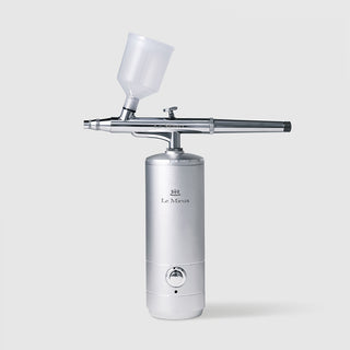 Le Mieux IOI Ionized Oxygen Infuser professional at-home skincare device silver handheld airbrush with cylindrical base power button adjustable precision nozzle and clear reservoir cup. Available at Art of Skin Care