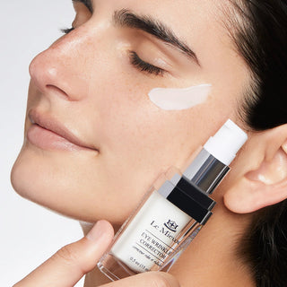 Model applying Le Mieux Eye Wrinkle Corrector 0.5 oz under eye area with product bottle held alongside face.