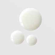 Le Mieux Oh My Glow Serum three opaque white milky serum drops in varying sizes showing lightweight fluid texture on grey background