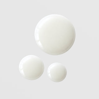 Le Mieux Oh My Glow Serum three opaque white milky serum drops in varying sizes showing lightweight fluid texture on grey background