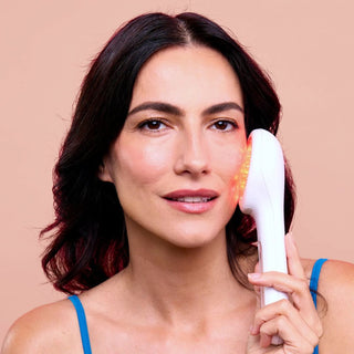 Woman with brown hair holds lightstim for wrinkles against cheek