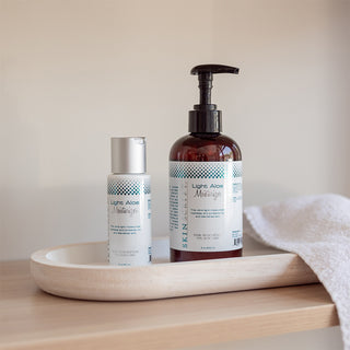 A stylized shot of Light Aloe moisturizer in both sizes sitting on a wooden tray with a white towel.