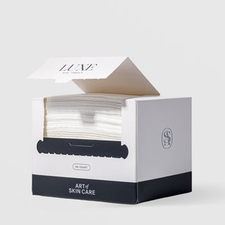 Art of Skin Care Luxe Eco Towels 50-count box open and dispensing soft white towels through a serrated tear slot, with the AS monogram logo on the side, displayed against a light gray background.