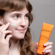 Woman applying GlyMed Plus Acne Mattifying Sulfur Masque to cheek while holding the orange tube