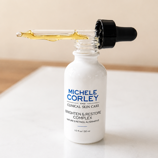 Michele Corley Clinical Skin Care Brighten and Restore Complex 1 oz dropper bottle open showing golden retinol alternative serum on marble surface.