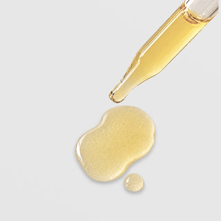 Michele Corley Brighten and Restore Complex texture showing light golden yellow botanical oil serum drops from glass dropper on grey background.
