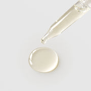 Michele Corley Calm Nourish and Repair Oil texture showing lightweight clear pale yellow facial oil drop from glass dropper on grey background.