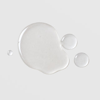 Michele Corley Calming Cleansing Oil and Makeup Remover texture showing lightweight clear oil droplets on grey background.