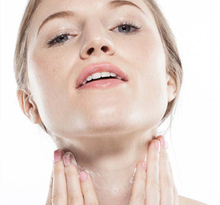 A woman applying Farmhouse Fresh Moon Dip Back to Youth Ageless Body Mousse to her neck and décolletage with both hands, against a white background.
