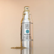 NeoGenesis Recovery Serum with serum dripping down and puddling next to the bottle on a beige background