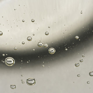 Macro closeup of NeoGenesis Recovery Serum showing lightweight clear gel formula with suspended micro-droplets and bubbles on neutral background