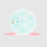 Omnilux Mini Blemish Eraser LED device in a round shape with a white and teal floral line pattern, power button, and visible red LED light glow along the bottom edge, displayed against a light gray background.