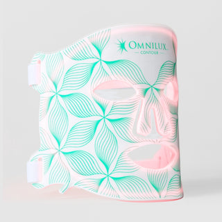 Omnilux Contour Face LED mask in white silicone with a teal floral line pattern, glowing pink through the eye, nose, and mouth openings, with white elastic head straps, displayed against a light gray background.