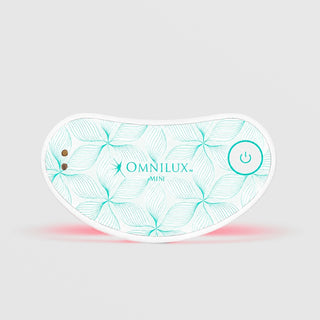 Omnilux Mini Eye Brightener LED device in a curved under-eye shape with a white and teal floral line pattern, power button, and visible red LED light glow along the bottom edge, displayed against a light gray background.