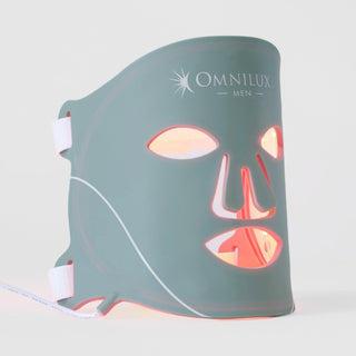 Omnilux Men LED face mask in slate teal silicone with white logo, glowing red and amber through the eye, nose, and mouth openings, with white elastic head straps, displayed against a light gray background.