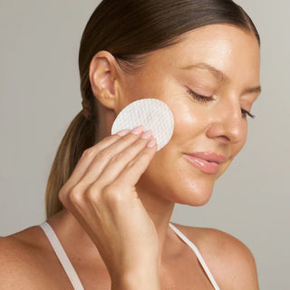 Woman sweeping a (plated) Exosome Enhancer Daily Prep Pad across her cheek to prep skin for exosome serum