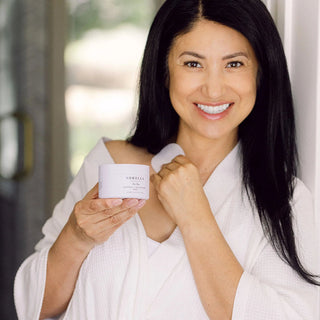 Smiling woman in a white robe holding Sorella Apothecary Mandelic + Willow Bark Peel Pads Step 1 jar