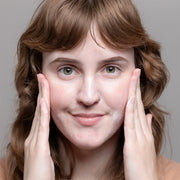 Woman massaging GlyMed Plus Elite Peptide Firming Cleanser onto face with both hands