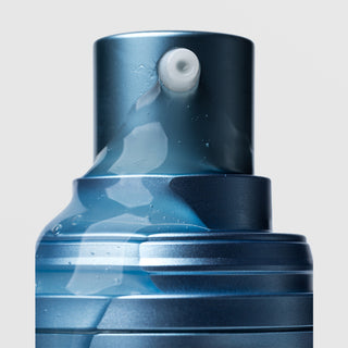 Close-up of Plated Skin Science CALM Serum pump nozzle dispensing lightweight clear gel serum with micro-bubbles on blue metallic bottle