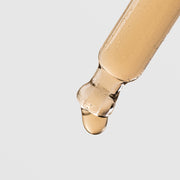 Close-up of Plated Hair Science Hair Serum dropper tip dispensing a single drop of lightweight golden serum