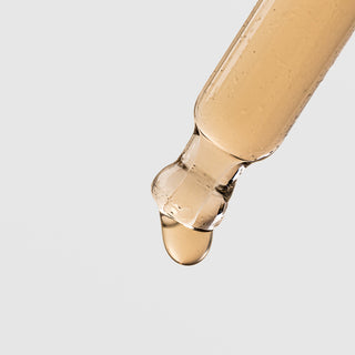 Close-up of Plated Hair Science Hair Serum dropper tip dispensing a single drop of lightweight golden serum