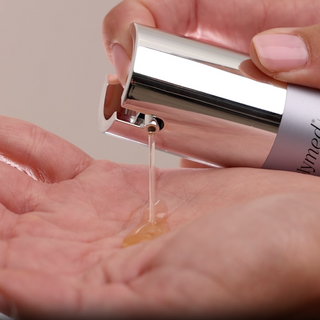 Dispensing GlyMed Plus Restoring Fulvic Elixir amber-toned serum from silver pump applicator into palm of hand