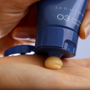 Squeezing GlyMed Plus Vitamin C Cream from navy blue tube onto back of hand showing rich yellow cream texture