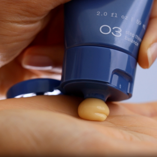 Squeezing GlyMed Plus Vitamin C Cream from navy blue tube onto back of hand showing rich yellow cream texture