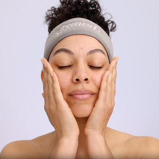 Model pressing GlyMed Plus Revitalizing Essence with NAD+ into cheeks wearing branded GlyMed headband