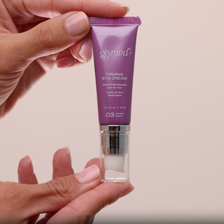 Hands holding GlyMed Plus Elite Firming Eye Cream 10mL purple pump tube