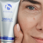 Woman with silver hair and blue eyes holding iS Clinical Sheald Recovery Balm tube beside her glowing skin