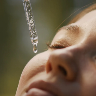 Close-up of a serum dropper dispensing a drop onto a woman's face with eyes closed