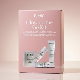 Sente Glow on the Go Kit travel size skincare set in a pink box, featuring a serum packet, tube, and bottle with white and blue labels, displayed on a reflective surface against a soft pink background.