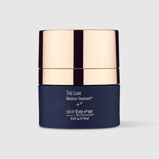 A dark navy blue cosmetic jar with a reflective metallic rose gold lid, labeled 'Trio Luxe Moisture Treatment' by skinbe+ter SCIENCE, on a light gray background.