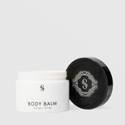 Sorella Apothecary Body Balm 6 fl oz open white jar showing cream texture beside black ornate lid on a light gray background