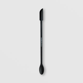 Sorella Apothecary Good to the Last Drop dual-ended black spatula with flat blade on one end and spoon on the other on a light gray background