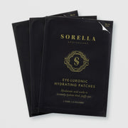 Three packets of Sorella Apothecary Eye-Luronic Hydrating Patches in black and gold foil packaging on a light gray background