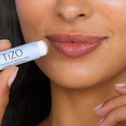 Woman applying TiZO Tinted Lip Protection Mineral Sunscreen SPF 45 lip balm stick showing tinted hydrated lips