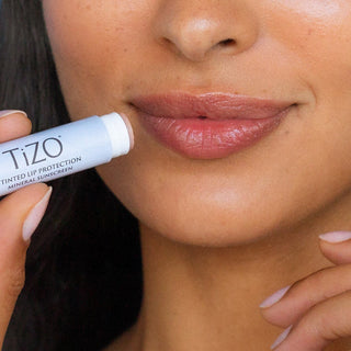 Woman applying TiZO Tinted Lip Protection Mineral Sunscreen SPF 45 lip balm stick showing tinted hydrated lips
