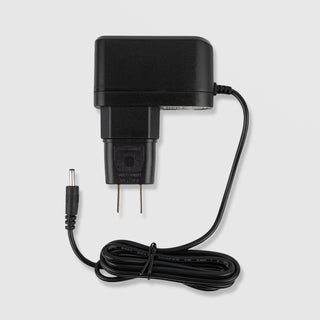 Time Master Pro replacement AC power adapter charger black wall plug with DC barrel connector and coiled cable on grey background