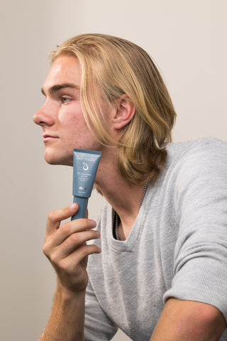 Young man with acne-prone skin holding Face Reality 8% L-Mandelic Serum – exfoliating brightening serum for acne-prone skin
