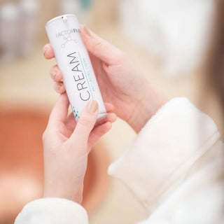 Woman in bathrobe holding FactorFive Anti-Aging Cream bottle during skincare routine