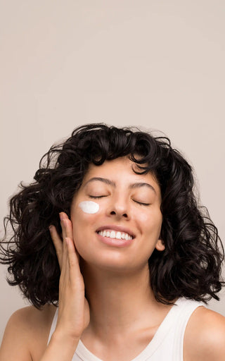 Woman smiling with skincare cream applied to her cheek — Art of Skin Care Clear Skin Coaching