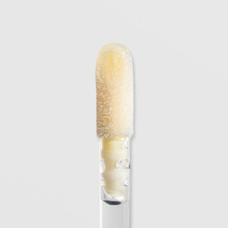Close-up of Rhonda Allison LumiColour Lip Restore Serum doe-foot applicator loaded with pale yellow lip serum formula on a light gray background
