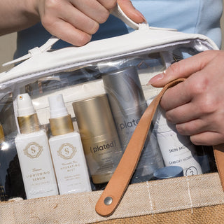 Model placing Art of Skincare Signature Cosmetic Case into a tote bag, case filled with assorted skincare products including Sorella and Plated serums