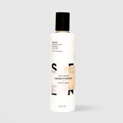 SEEN Skin-Caring Conditioner (8.6 fl oz) in a white bottle with a black flip cap and bold SEEN lettering accented by a warm tan color block, labeled dermatologist designed and suitable for all hair types, displayed against a light gray background.