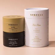 Sorella Apothecary Vitamin C + Ferulic Peel Pads two-step set with gold and black jars beside the white cylindrical gift box on a warm beige background