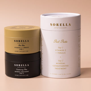 Sorella Apothecary Vitamin C + Ferulic Peel Pads two-step set with gold and black jars beside the white cylindrical gift box on a warm beige background
